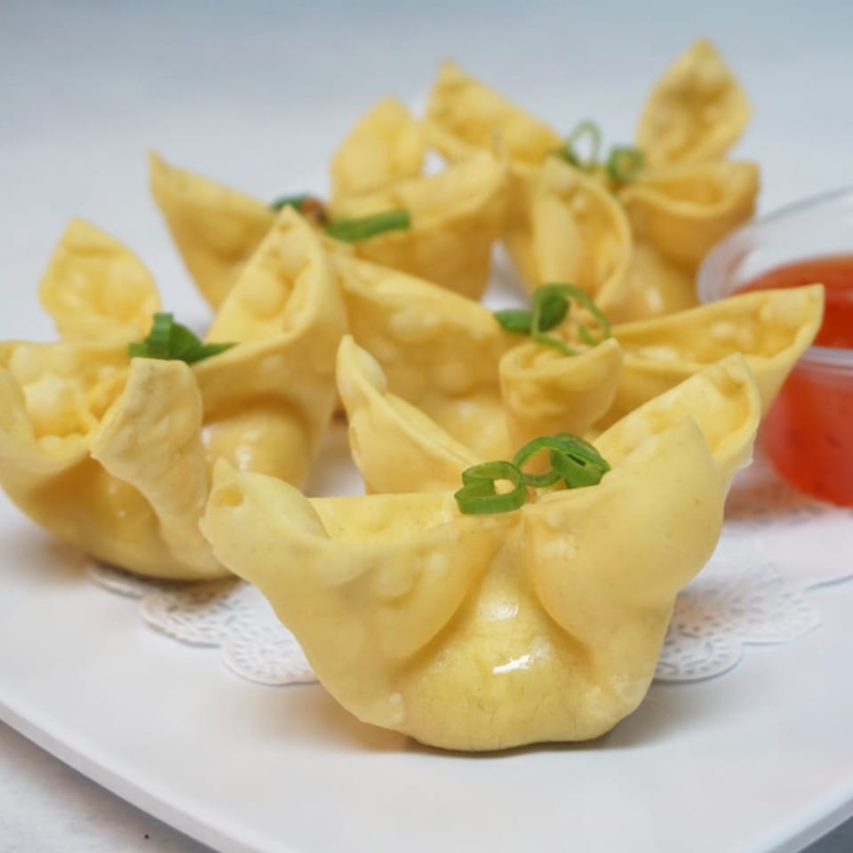 Golden crab rangoon appetizers, garnished with green onions, served with a side of sweet chili sauce.