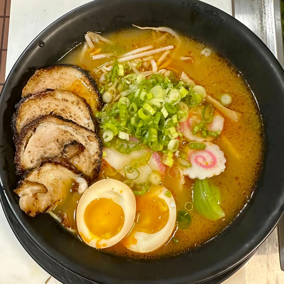 A black bowl of Grille One Nine Asian Fusion ramen with pork, egg, scallions, and fish cake.