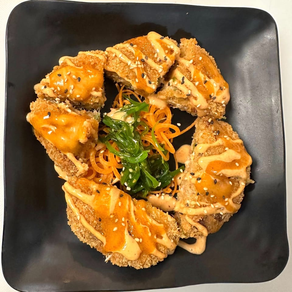 Fried sushi rolls with orange sauce and sesame seeds, garnished with seaweed salad and shredded carrots.
