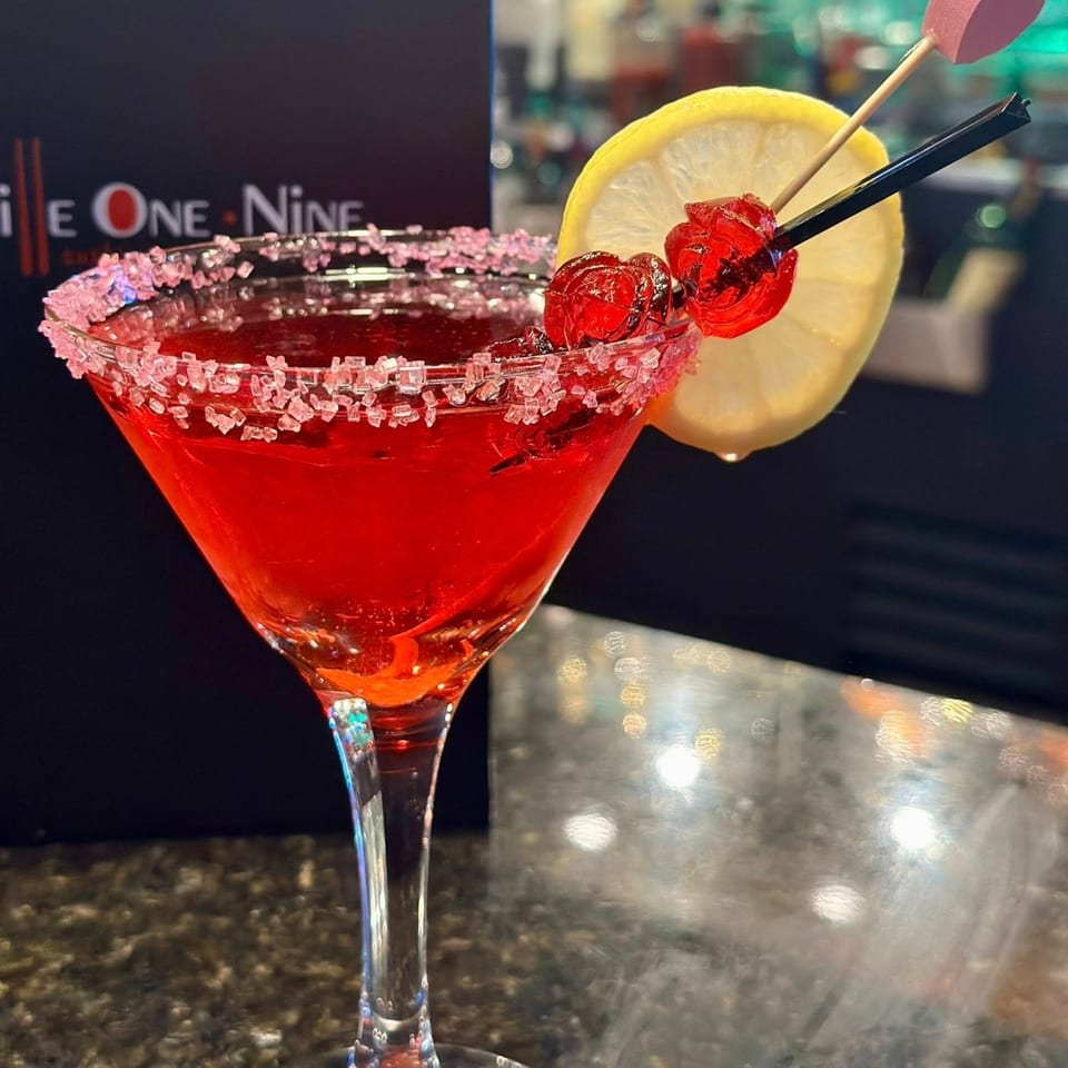 Red cocktail with a sugar-rimmed glass, garnished with a lemon slice and cherries at Grille One Nine.