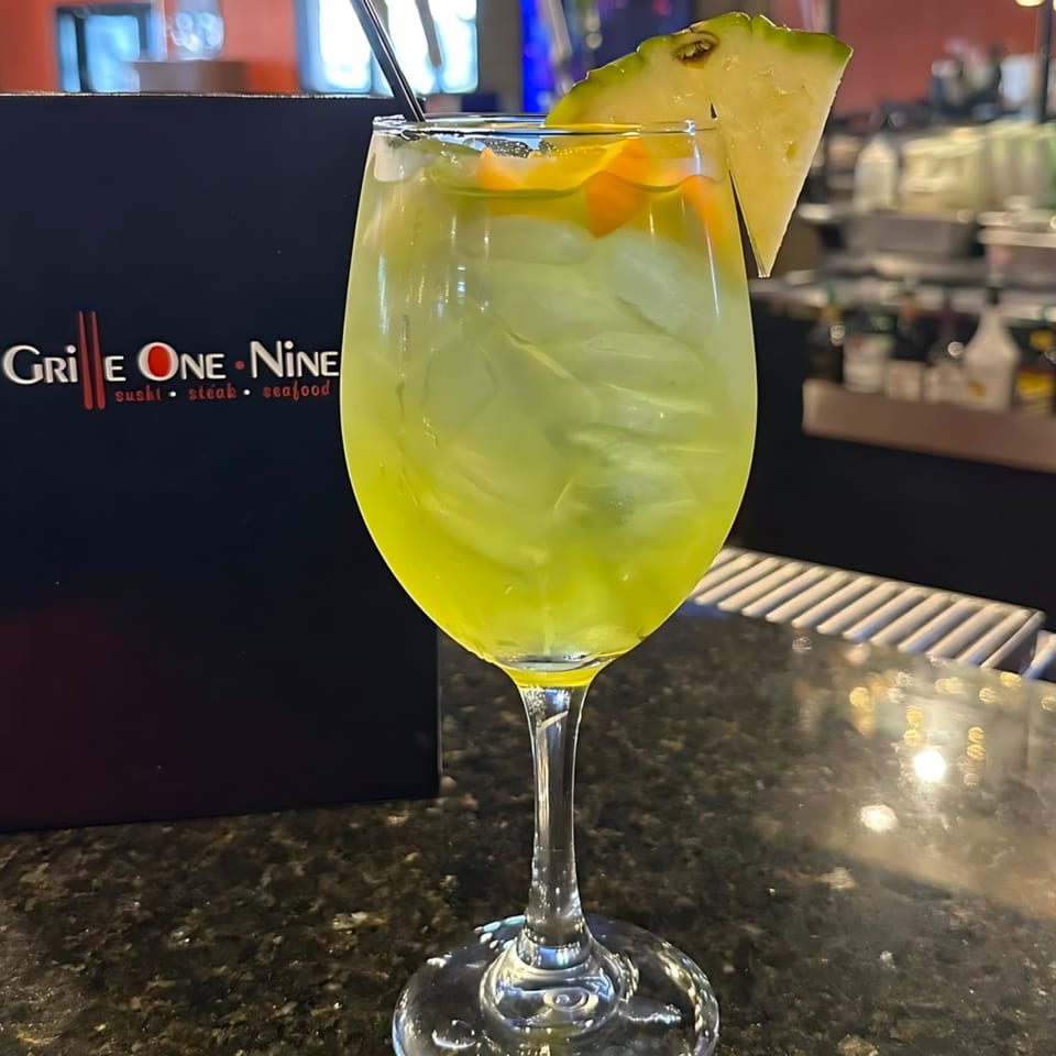 A vibrant green cocktail with ice, orange slices, and a pineapple wedge, on a bar counter.